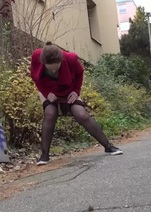 Caucasian female Lora takes a piss while walking on a pathway in the city