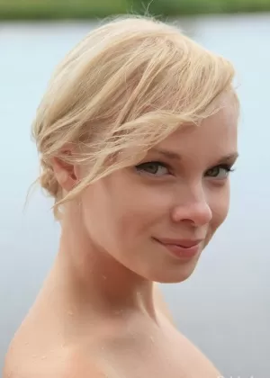 Красивая блондинка Феона ест арбуз, позируя обнаженной на причале у озера