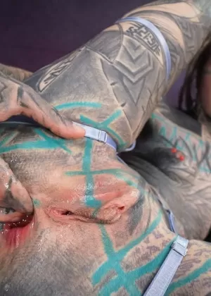 Heavily tattooed girl fingers her asshole while giving a blowjob