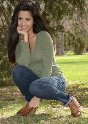 Латиноамериканка Белла Куинн взбирается на дерево в парке в свитере и джинсах