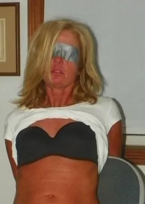 Светловолосую женщину связывают веревкой после того, как ей завязали глаза и заткнули рот кляпом