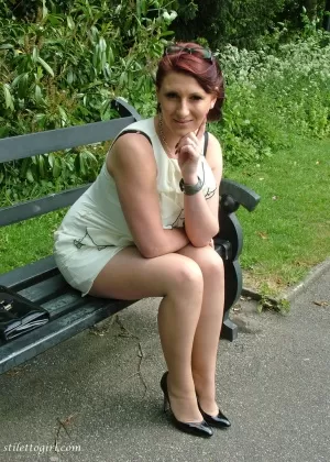 Толстая женщина в очках демонстрирует свои туфли на шпильках на скамейке в парке